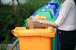 a woman dump a plastic bottle garbage to yellow recycle bin in a park