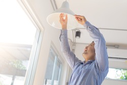 Asian man changing light bulb in coffee shop , installing a fluorescent light bulb