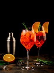 Wineglass of ice cold Aperol spritz cocktail served in a wine glass, decorated with slices of orange and rosemary branch. Black background. Copy space
