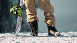 Close up of snowboard boots with snowboarder and snowboard standing in snow