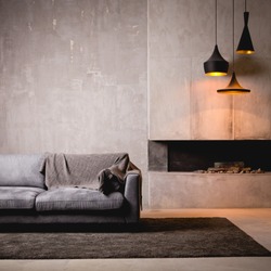 Gray velour sofa in a dark room the bright light from eternal light, and artificial fireplace. Interior loft with concrete walls