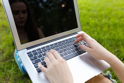 Top view of woman sitting in the park on the green grass with laptop, her hands on keyboard. Student studying outdoors concept
