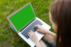 Top view of woman sitting in the park on the green grass with laptop, her hands on keyboard. Student studying outdoors concept