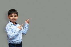 Smiling happy boy pointing finger away at copy space isolated over plain background