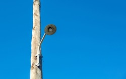 Retro streetlight, bulb hanging on wooden electric pole. Vintage pillar with lamp. Clear empty blue sky background, copy space.