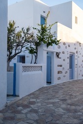 Greece, Ano Koufonisi island. Traditional stonewall building with tree, white and blue color facade, Cyclades architecture. Empty cobblestone street. 