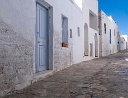 Greece, Ano Koufonisi island. New and aged traditional stonewall building, in white and blue color Cyclades architecture. Empty cobblestone street, blue sky background.
