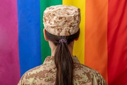 American army female soldier in USA military digital pattern uniform, looking at lgbt flag. United States, camo uniform, rainbow flag, love symbol in army. 