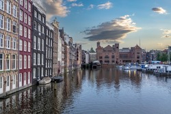 Amsterdam houses, reflections in canal water, blue sky at dusk. Touristic district Damrak, Netherlands Holland