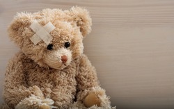 Child trauma concept.Teddy bear with bandage on head sitting on a wooden background. Copy space