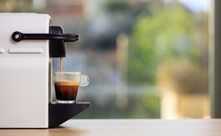 Morning capsule coffee. Espresso maker machine on a wooden table. Blurred background, space for text, front view