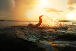 Swimmer conducts training in a lake at sunset after the rain. From under hands fly spray. Lens flare effect