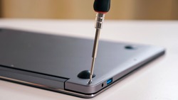Close-up of unscrewing bolts with a screwdriver on a silver laptop.