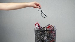 Woman throws out unnecessary glasses for eyesight on pile in rubbish bin against grey background as request to improve poor vision macro