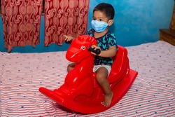 A boy wearing a surgical protective face mask and playing with a toy horse at home during coronavirus pandemic.