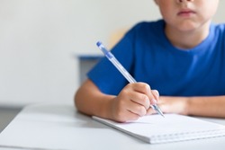 Writing hand of school child on lesson. Pupil sitting at desk in classroom. Kid studying in elementary college. Primary student back to school. Education for children. Close up of pen and copybook