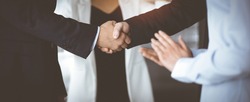 Unknown businesspeople are shaking their hands after signing a contract, while standing together in a sunny modern office, close-up. Business communication, handshake, and marketing concept