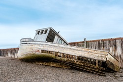 A wrecked boat on the shore next to an old wharf. The boat is in very poor shape and is falling apart. Low tide.