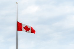 A Canadian flag at half mast, lowered in remembrance of the indigenous children who were abused and died in residential schools. Overcast, wide view.