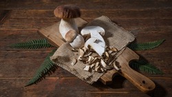 Dark food photography background - Forest mushrooms Boletus edulis (king bolete) penny bun cep porcini mushroom and fern on old wooden cutting board on table	
