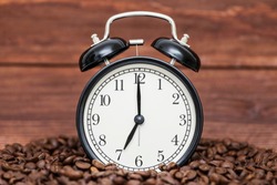 Alarm clock and coffee beans on a wooden background. Alarm clock standing on the beans of coffee. Coffee time concept