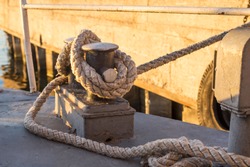 Tied rope knot on metallic bollard , seafaring port. Nautical ship moored in dock. Anchor rope in the port, ship mooring tool.