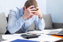 Distressed young man sit at desk paying bills feel stressed having financial problems. Unhappy upset male frustrated by debt or bankruptcy managing household budget or expenses.