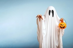 A white ghost with black eyes, made from a bedsheet with pumpkin basket