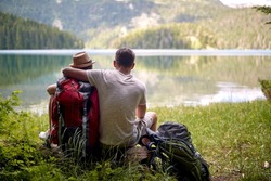 Couple on hike. Hugging and sitting in front of lake with backpacks. Hiking, lifestyle, recreation concept