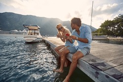 Man and woman sitting on the lake pier dangling legs and eat watermelon  together