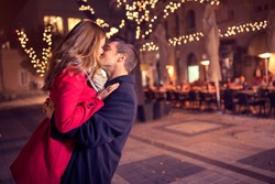 Young affectionate couple kissing tenderly on Christmas street 