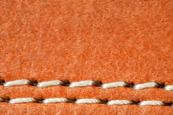 Leather is natural orange, seam is made of white threads, close-up macro view