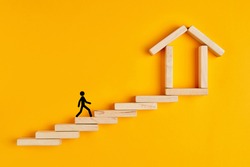 Male stickman climbing the ladders towards home formed by wooden blocks on yellow background.
