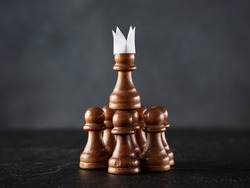 Group of a pawn team holding up a pawn with paper crown. Business entrepreneurship, teamwork, leadership choice concept.