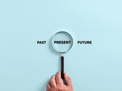 Male hand holds a magnifier focusing on the present time alongside the past and future. To focus on the current situation, positive thinking mindset concept.