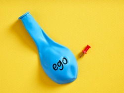 Deflated blue balloon with the word ego and a pin. Selfishness or regression of the extreme ego concept.