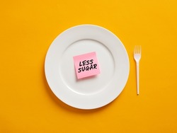 Notepaper with the word less sugar on a white plate. Less sugar intake and healthy nutrition concept.