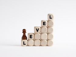 Level up or next level concept. Chess pawn is climbing the ladder of wooden cubes with the word level.