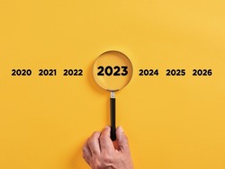 Male hand holds a magnifier focusing on the year 2023. Focus on new business goals, plan and strategy of the year 2023 concept.