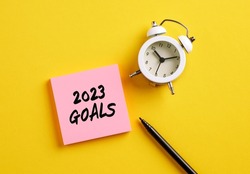 2023 goals message on pink note paper with alarm clock and pen. Planning personal or business goals for the year 2023.