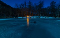 Beautiful winter night landscape. Frozen lake with crack on the ice, beautiful forest and small bonfire.  