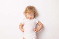 Caucasian curly baby girl in a white T-shirt on a white background hands holding a waist. child hands in hips.