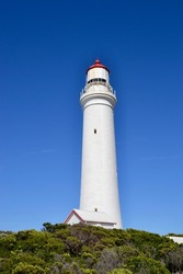 Low angle view of the Cape Nelson lighthouse on Australia's Victoria coast is white with a red dome against a cobalt blue sky