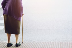 elderly old woman with walking stick stand waiting on footpath sidewalk crossing the street alone. concept senior across the street to zebra crosswalk.