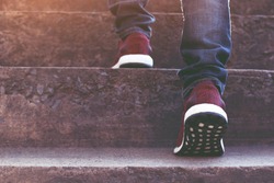stairway. Close up legs jeans and shoes sneakers red of young hipster man One person walking stepping going up the stairs in modern city, go up staircase, success, grow up. Sunshine in the morning.