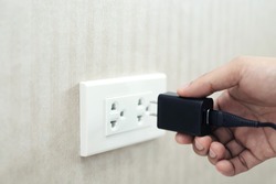 Hand ready to plug or unplug  black power cord cable mobile phone charger charts Into electric socket on wall. Ready to connect plugging electrical. power saving or cost reduction concept. soft focus.