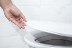 close up hand of a man closing the lid of a toilet seat. Hygiene and health care concept.