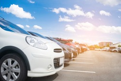 Car parked in large asphalt parking lot in a row with beautiful sky background. Outdoor parking lot with nature fresh ozone and green environment of travel transportation business concept