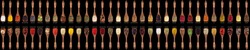  large collection of spices and herbs in wooden spoons. Seasonings for food isolated on a black background, top view.