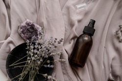 Glass brown spray bottle with organic cosmetics on gray fabric. Beauty blogging concept